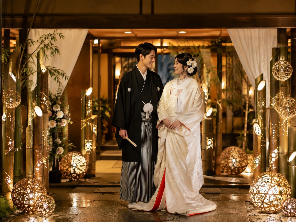 竹灯籠と竹鞠の光に包まれた会場入口で微笑む和装の新郎新婦