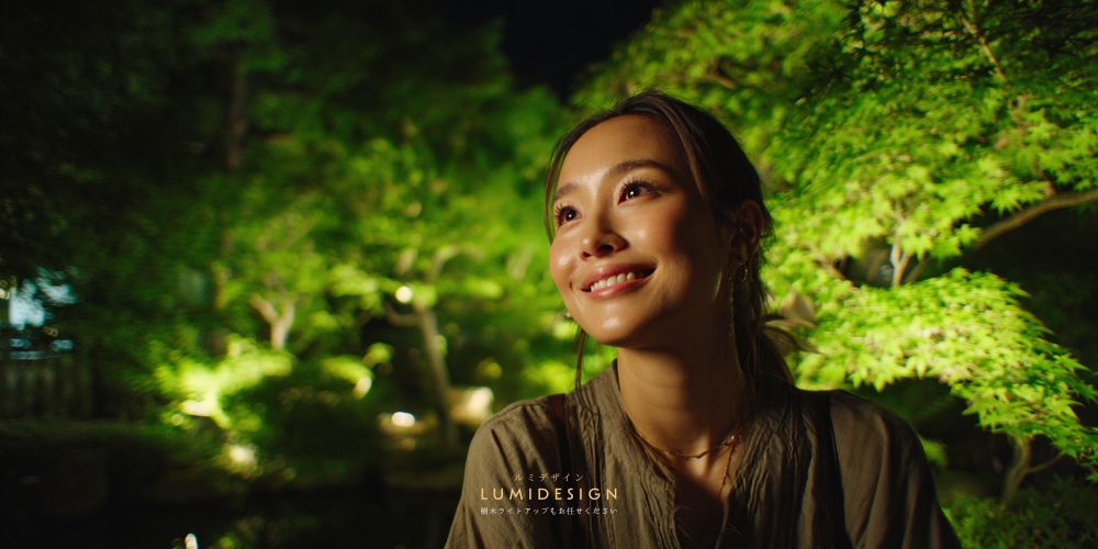 緑の木をライトアップした庭を見て感動する20代女性 屋外照明演出のイメージ
